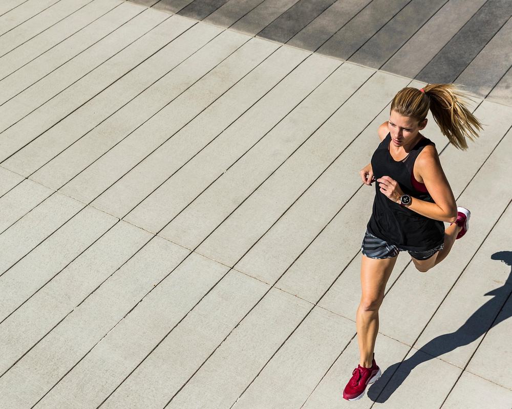 Vrouw loopt hard op een zonnig, betegeld plein tijdens haar training.